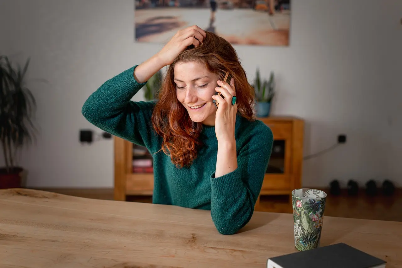 Stock photo: smiling woman with red hair on a phone call, sitting at a wooden table